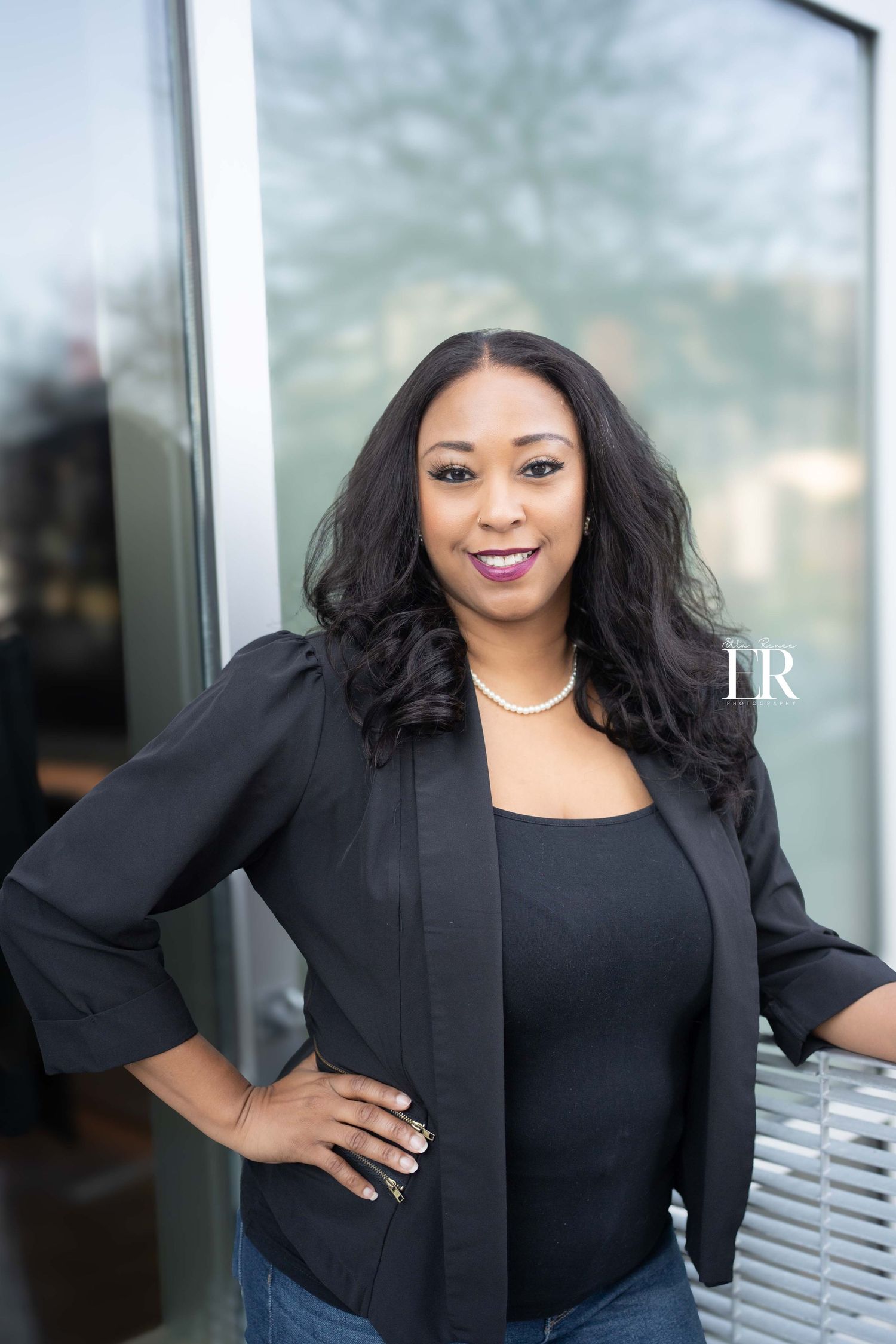 Business woman in black blazer poses confidently in modern office setting.