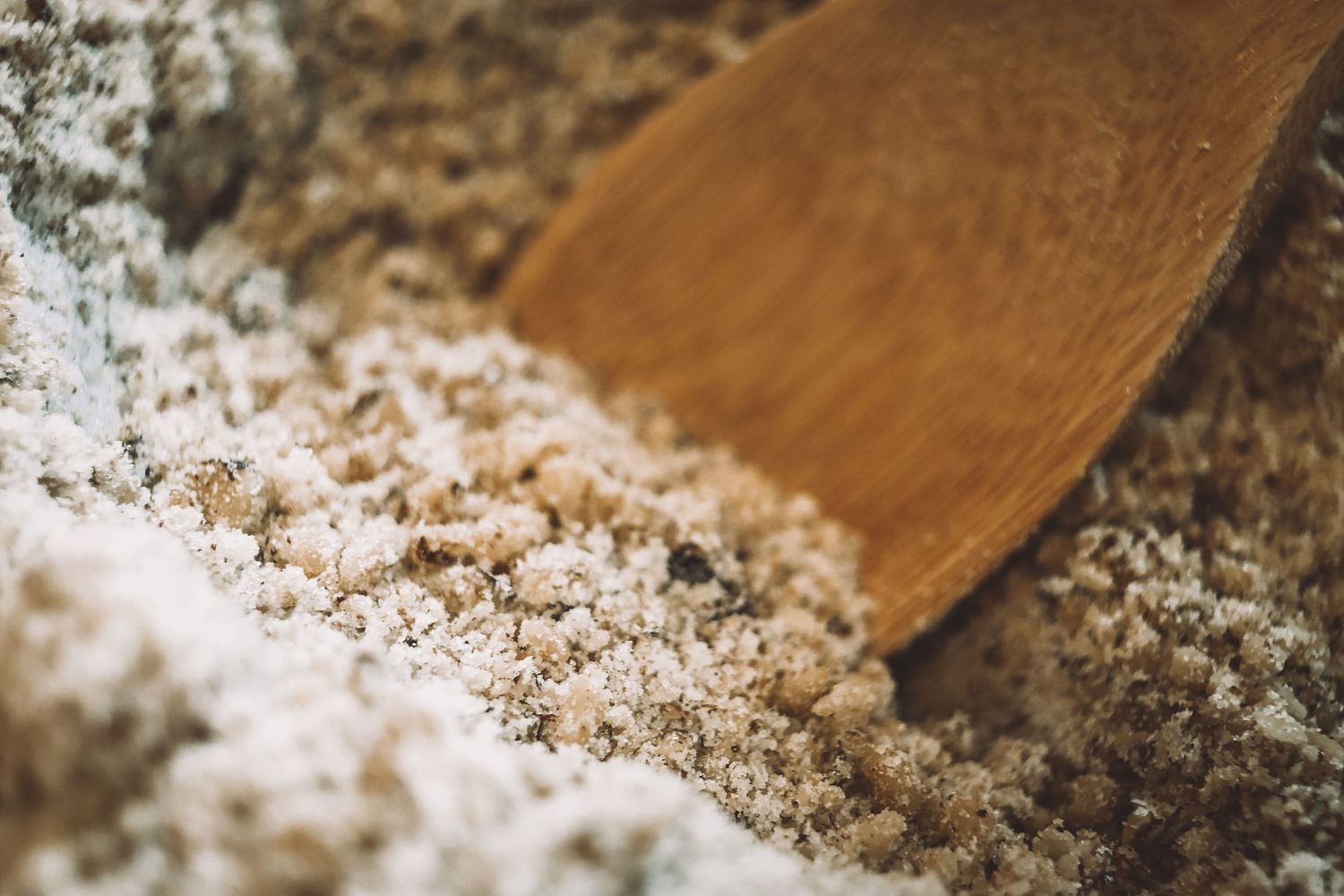 A wooden spoon rests beside a pile of coarse kosher or sea salt on a dark surface.