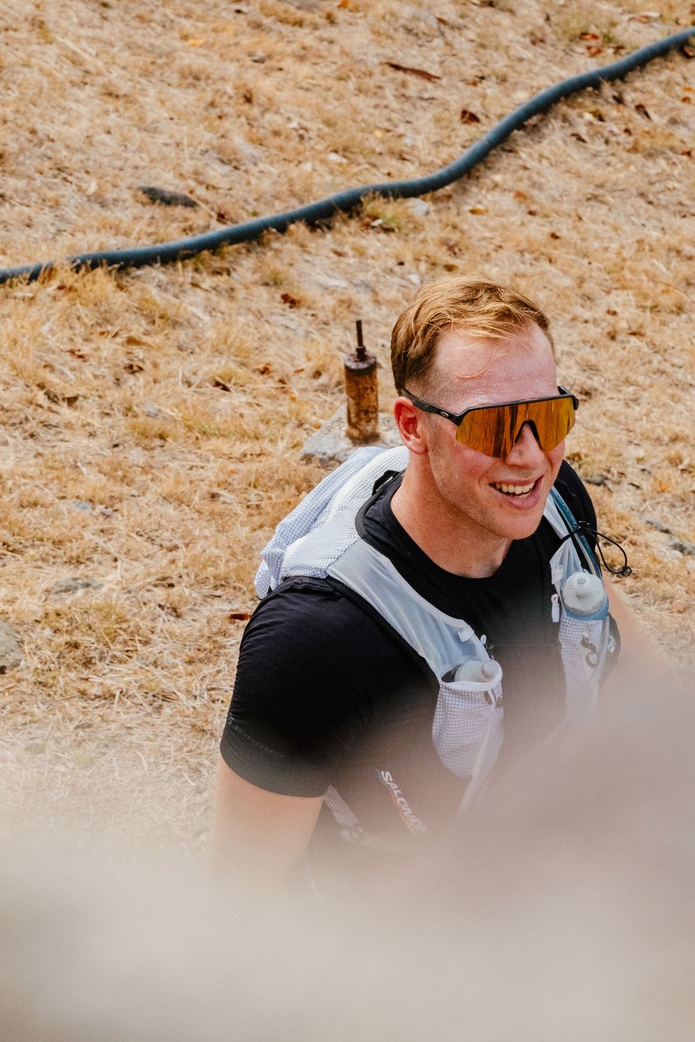Active hiker in sunglasses and backpack smiles while exploring outdoor trail on sunny day.