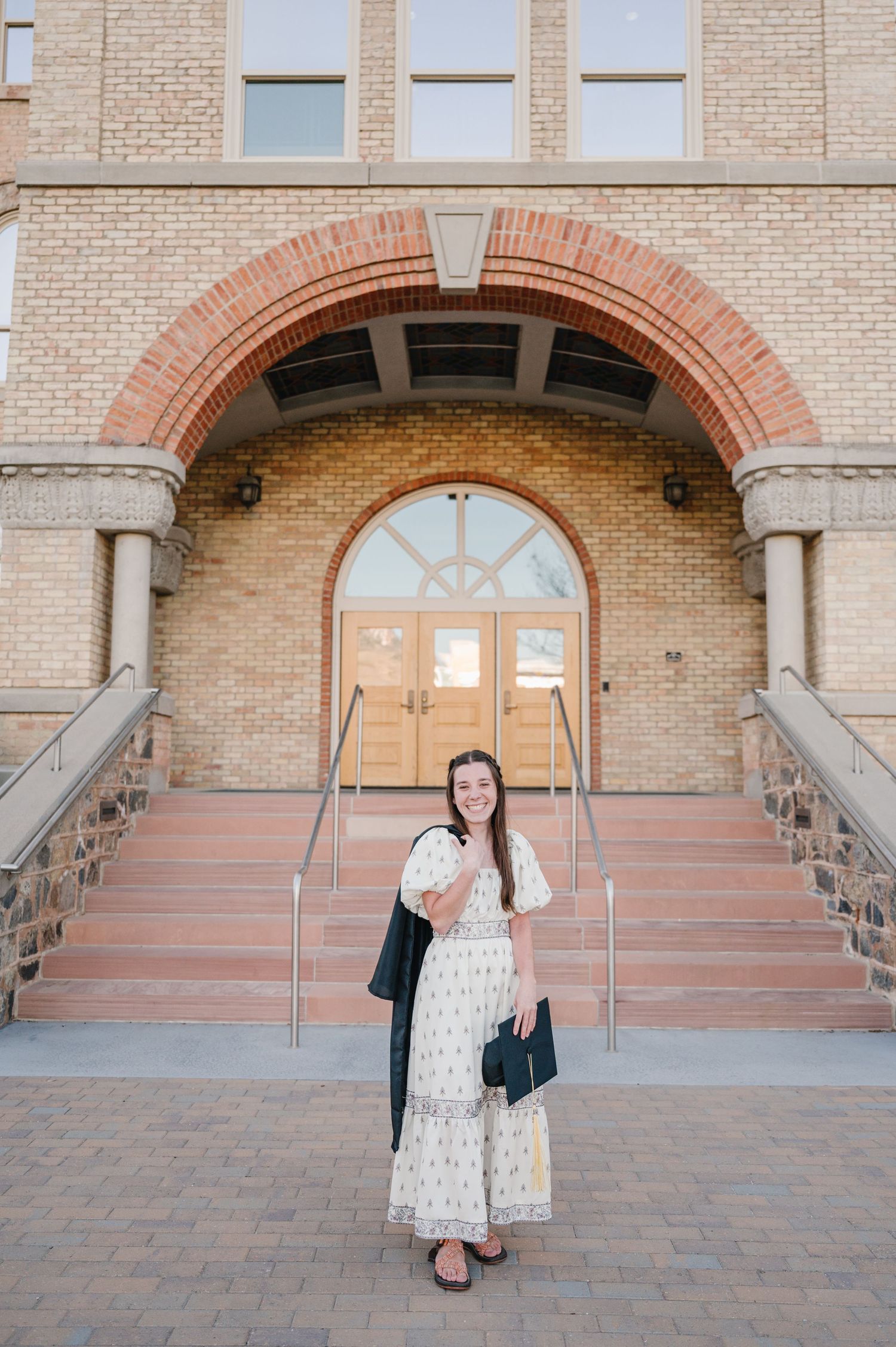 Someone in a white tiered maxi dress poses on stone steps in front of an arched brick entrance to a building.
