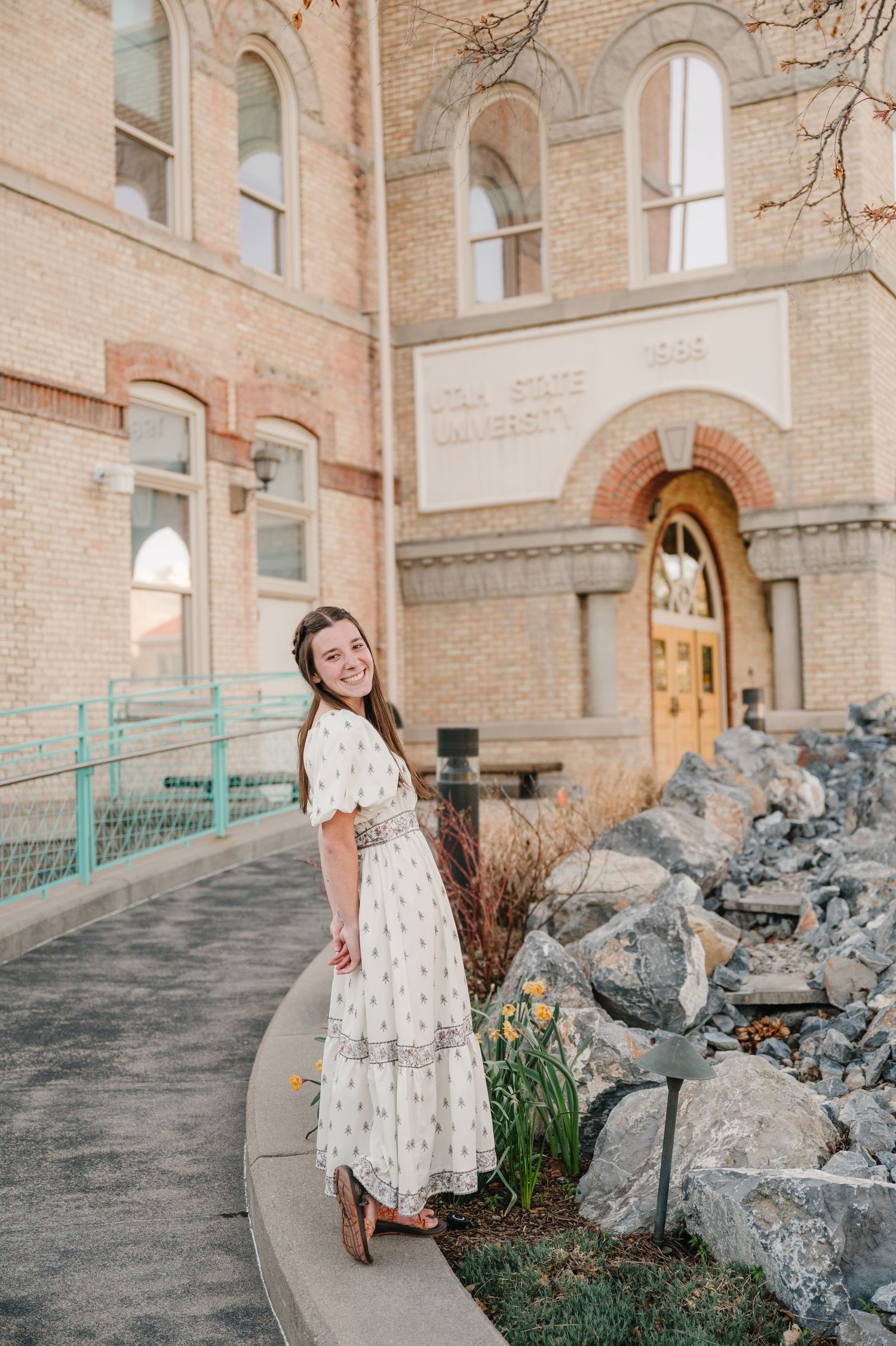 Stand in a flowy white vintage dress poses on a curved path outside a historic brick church building with arched windows.