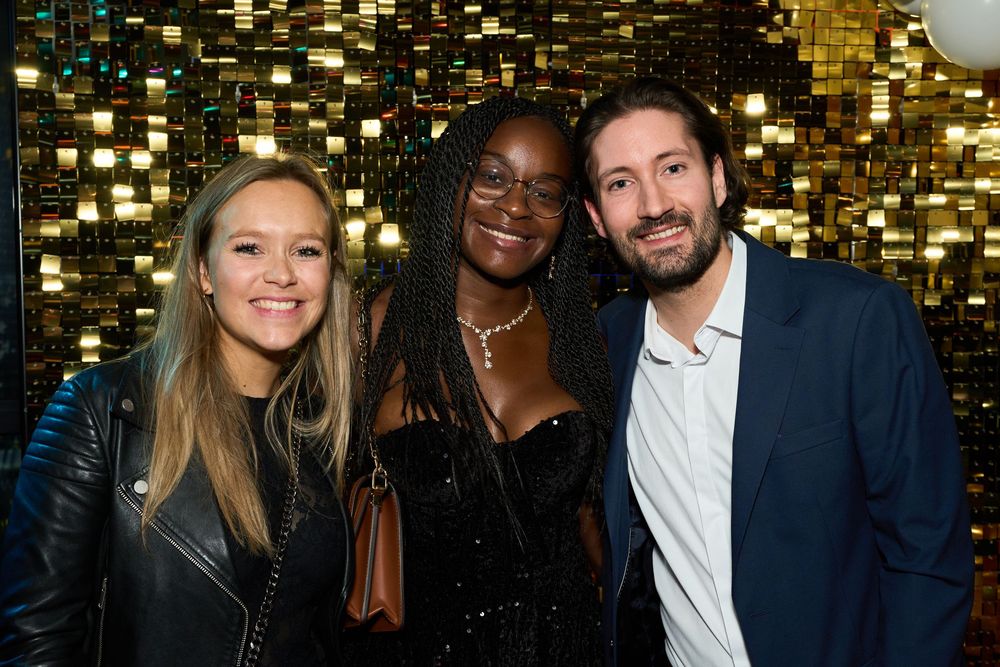 Trois amis posent ensemble lors d'un événement devant un fond doré scintillant.