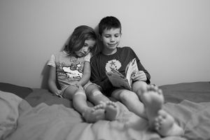 Deux enfants en train de lire une histoire dans leur lit, portrait en noir & blanc.