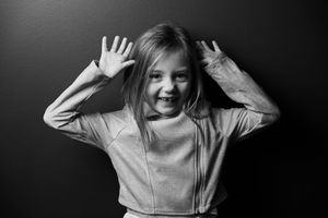 Portrait noir & blanc d'une fille joyeuse et souriante devant un fond obscur.