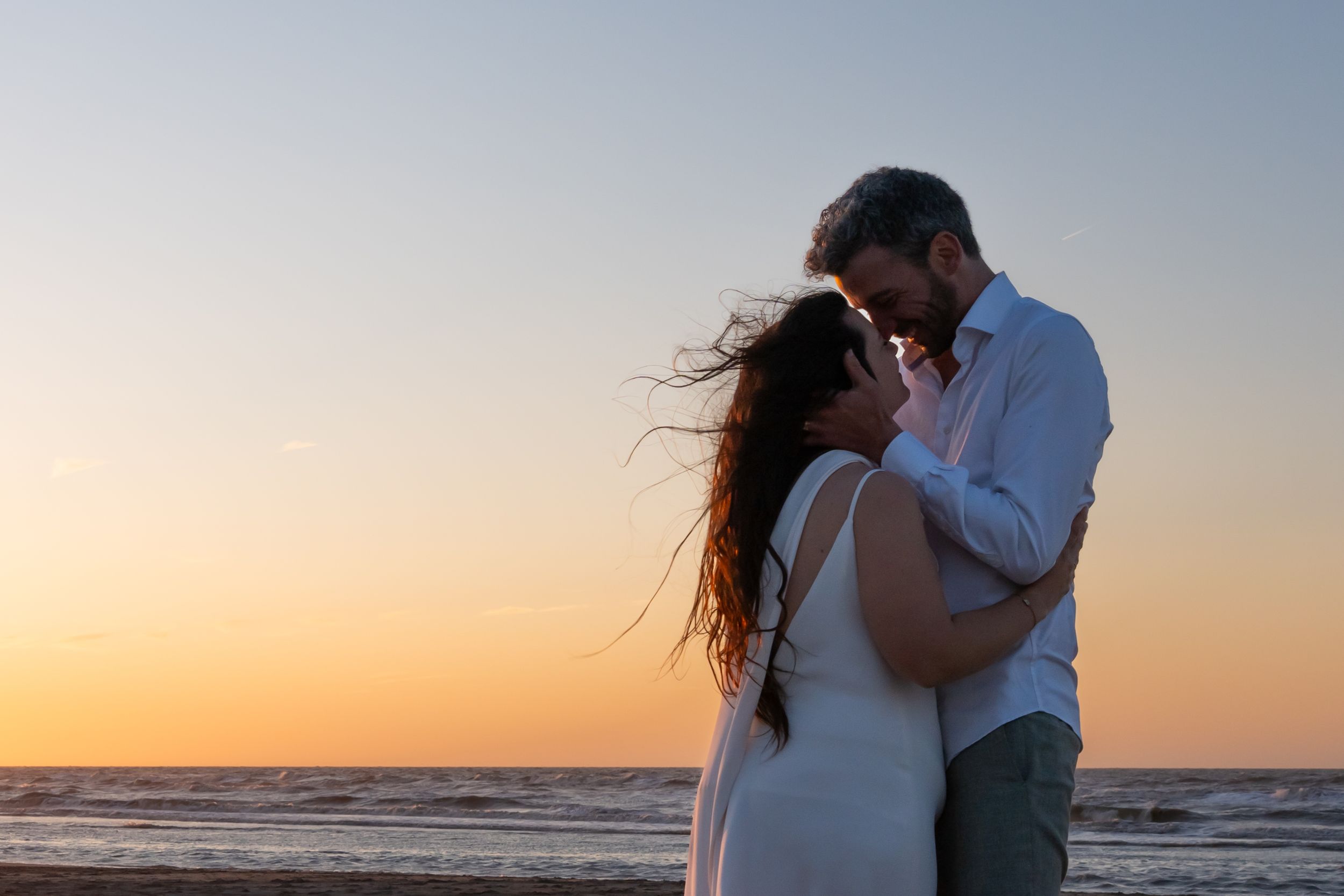 Un couple s'embrasse sur la plage au coucher du soleil tandis que les longs cheveux de la femme flottent dans la brise de l'océan.