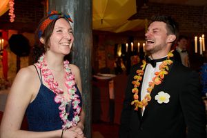Deux invités à une fête portant des leis floraux colorés partagent un rire joyeux lors d'une soirée.