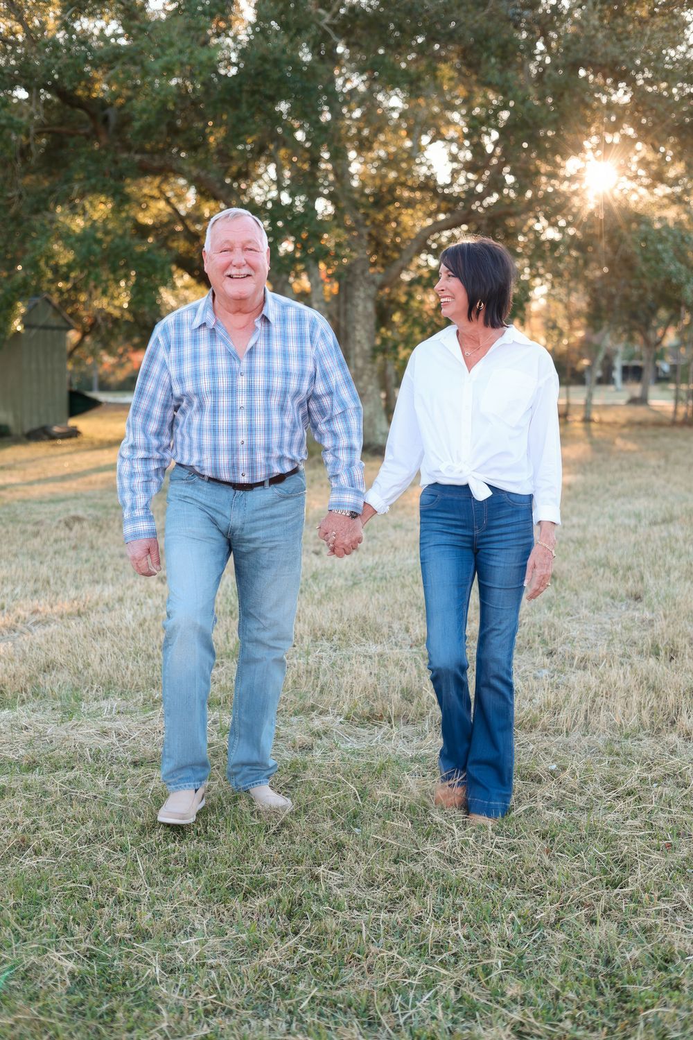 Couple walking hand in hand through a sunlit park at golden hour.