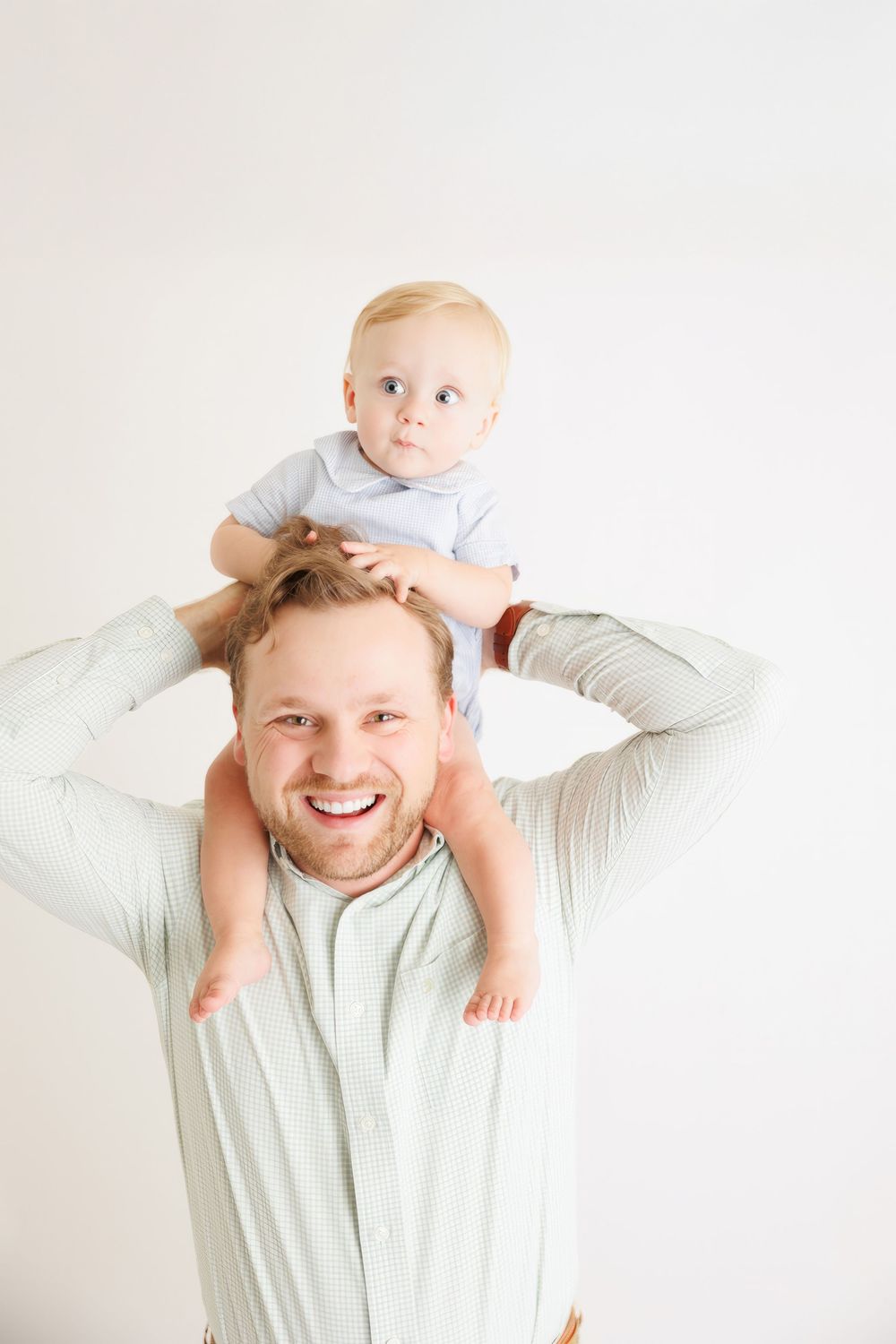 Smiling father holding baby on his shoulders against white background.