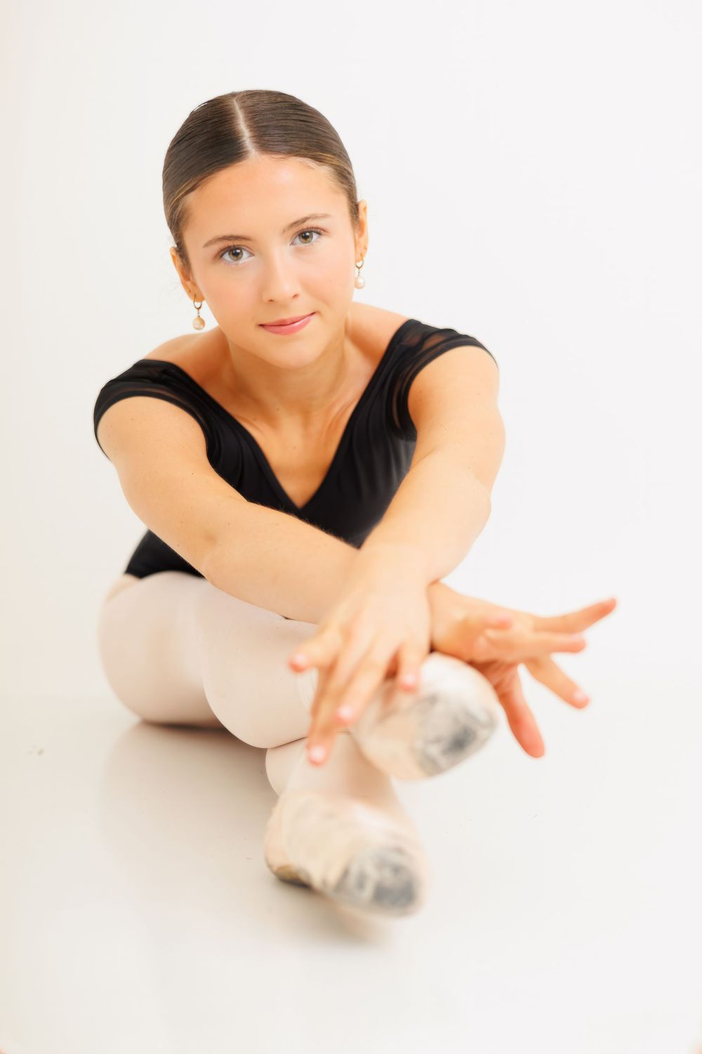 Ballet dancer in black leotard and white tights stretches gracefully on the floor in three elegant poses.