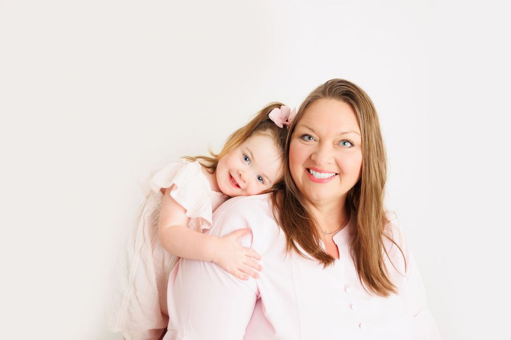A smiling woman and young girl in pink outfits pose together against a white background.
