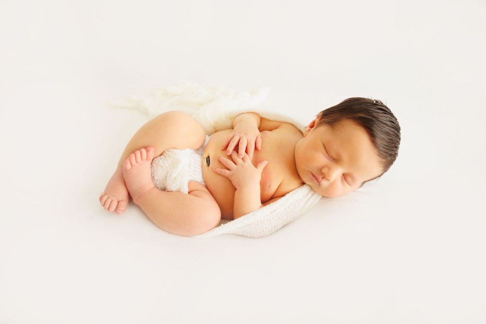 Peaceful newborn baby sleeping curled up on white blanket in professional studio photography pose.