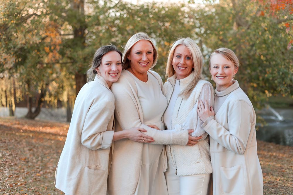 Group wearing coordinated cream outfits poses together during autumn photoshoot. Mother and daughter photography session.