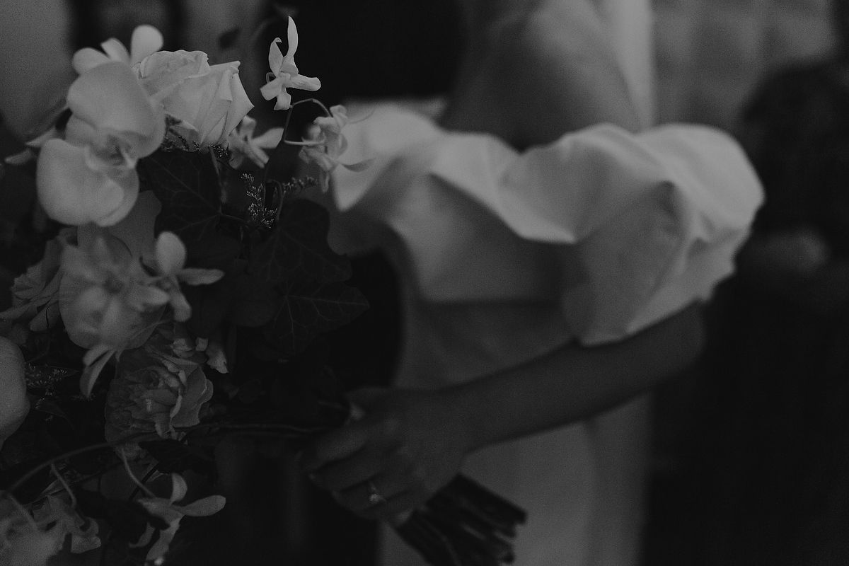 Black and white wedding photo of bride holding a lush floral bouquet with roses and orchids in elegant detail.