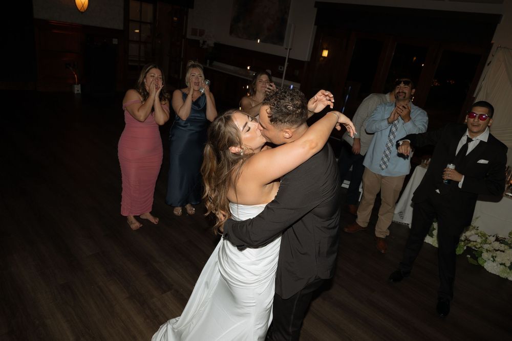 Bride and groom share first dance at wedding reception while guests cheer and celebrate in background.