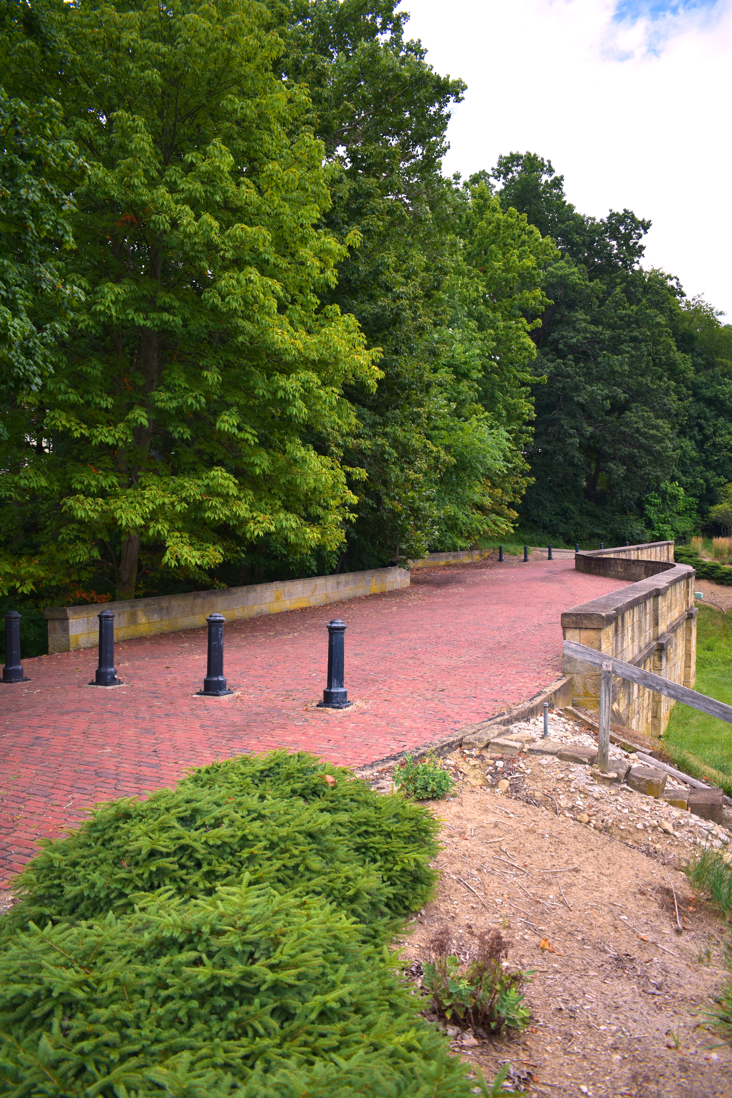 A brick paved pathway lined with green trees and metal posts on a sunny day.