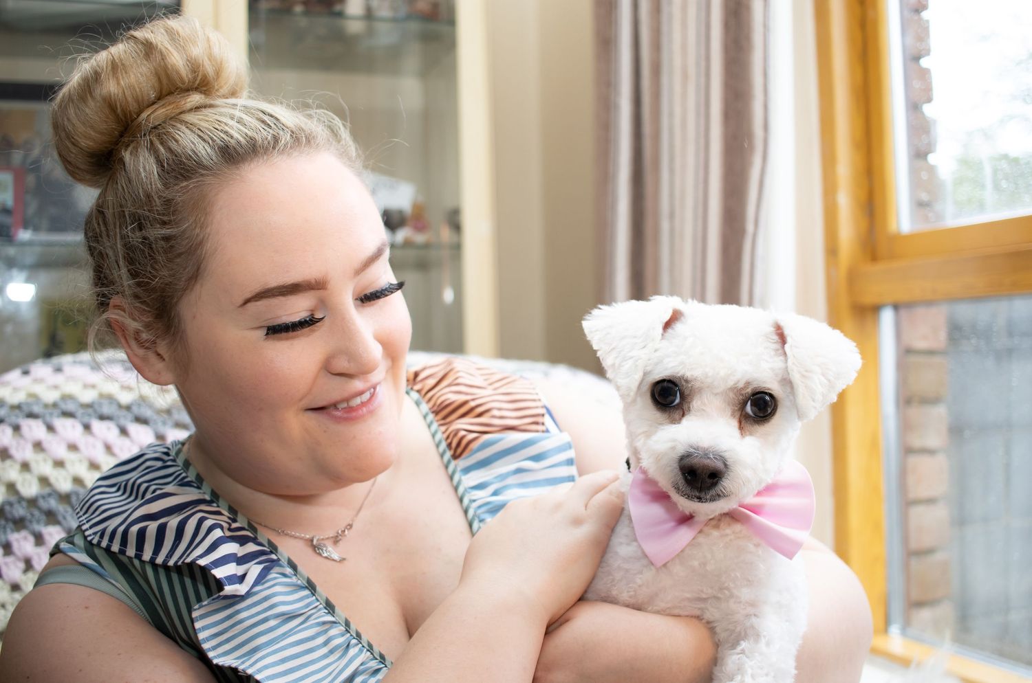 A person cuddles with their small white dog while relaxing at home.