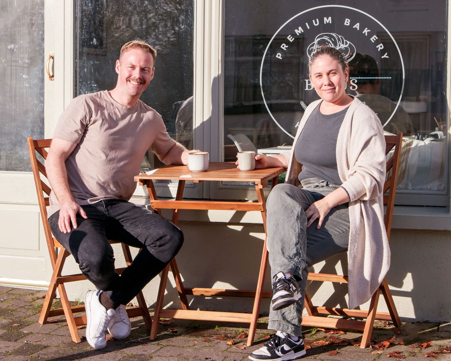 People relaxing on wooden chairs outside cafe storefront.