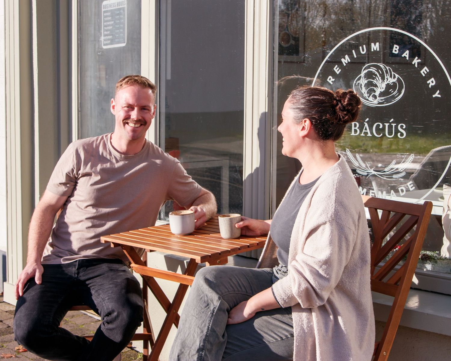 Customers enjoying coffee at outdoor tables of Bacus Cafe on sunny day.