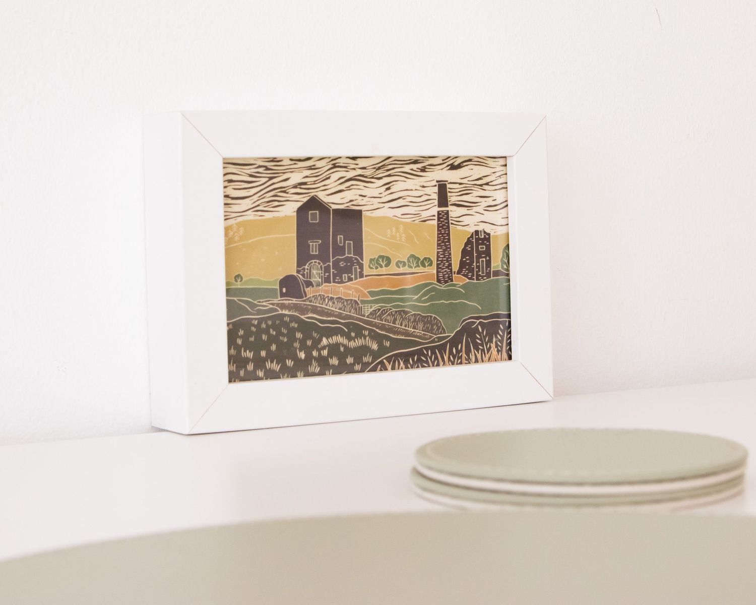 Minimalist shelf display with framed artwork and ceramic dishes against a white wall.