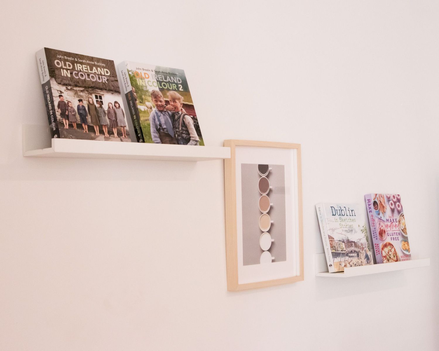 Collection of framed photographs displayed on white floating wall shelves.