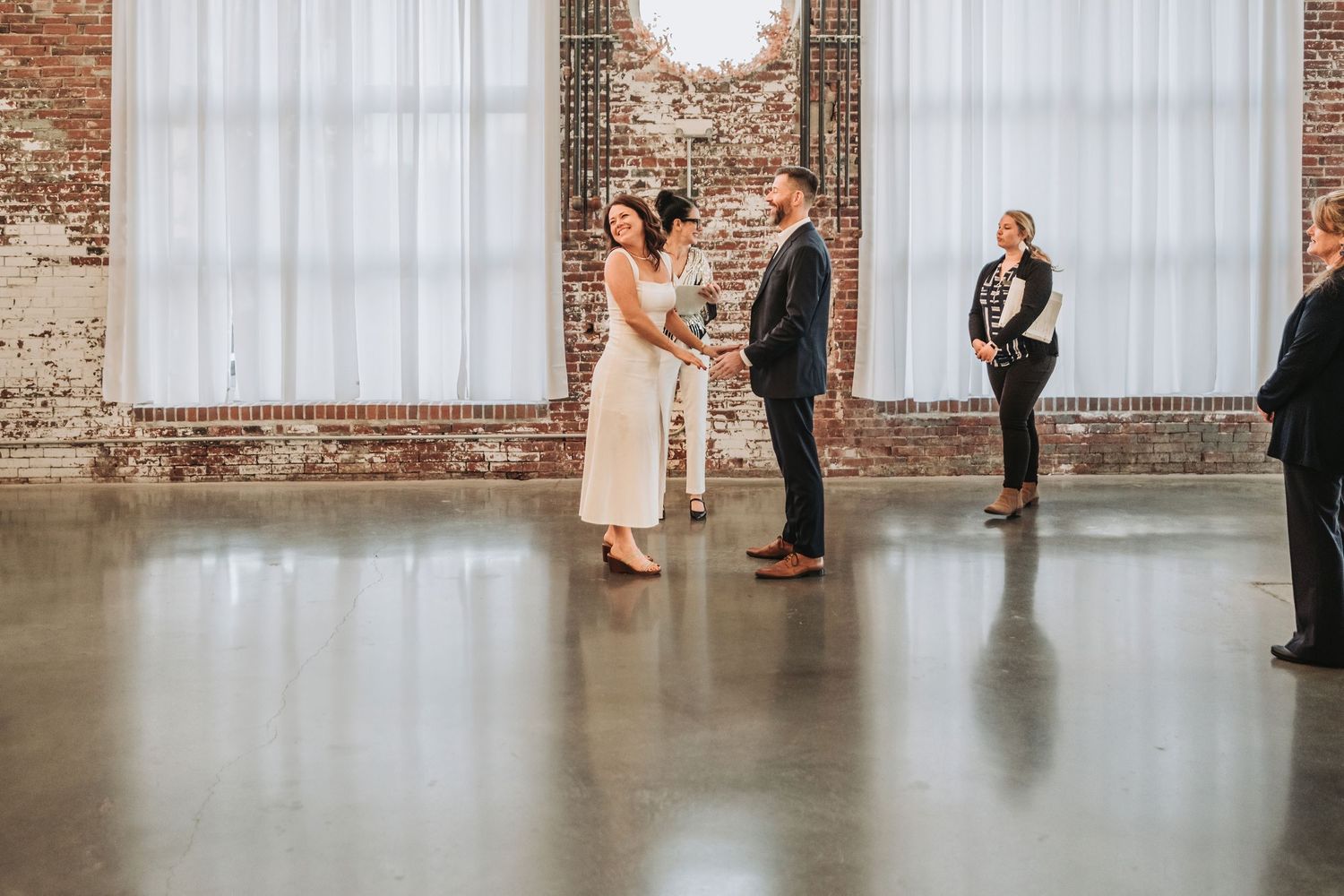 Two people stand together in ceremony at an industrial venue with exposed brick walls and polished concrete floors.  Halo at the Point.