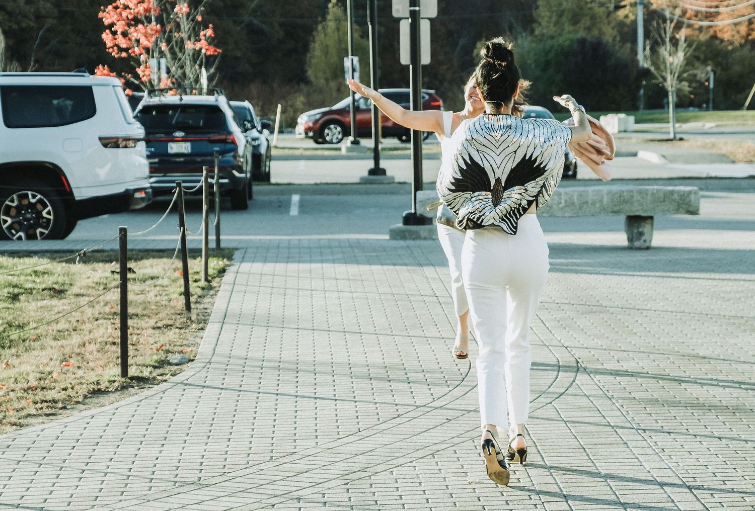 A friend dressed in white pants and a black and white patterned top runs to hug the bride-to-be at Halo at the Point in Portland, Maine.