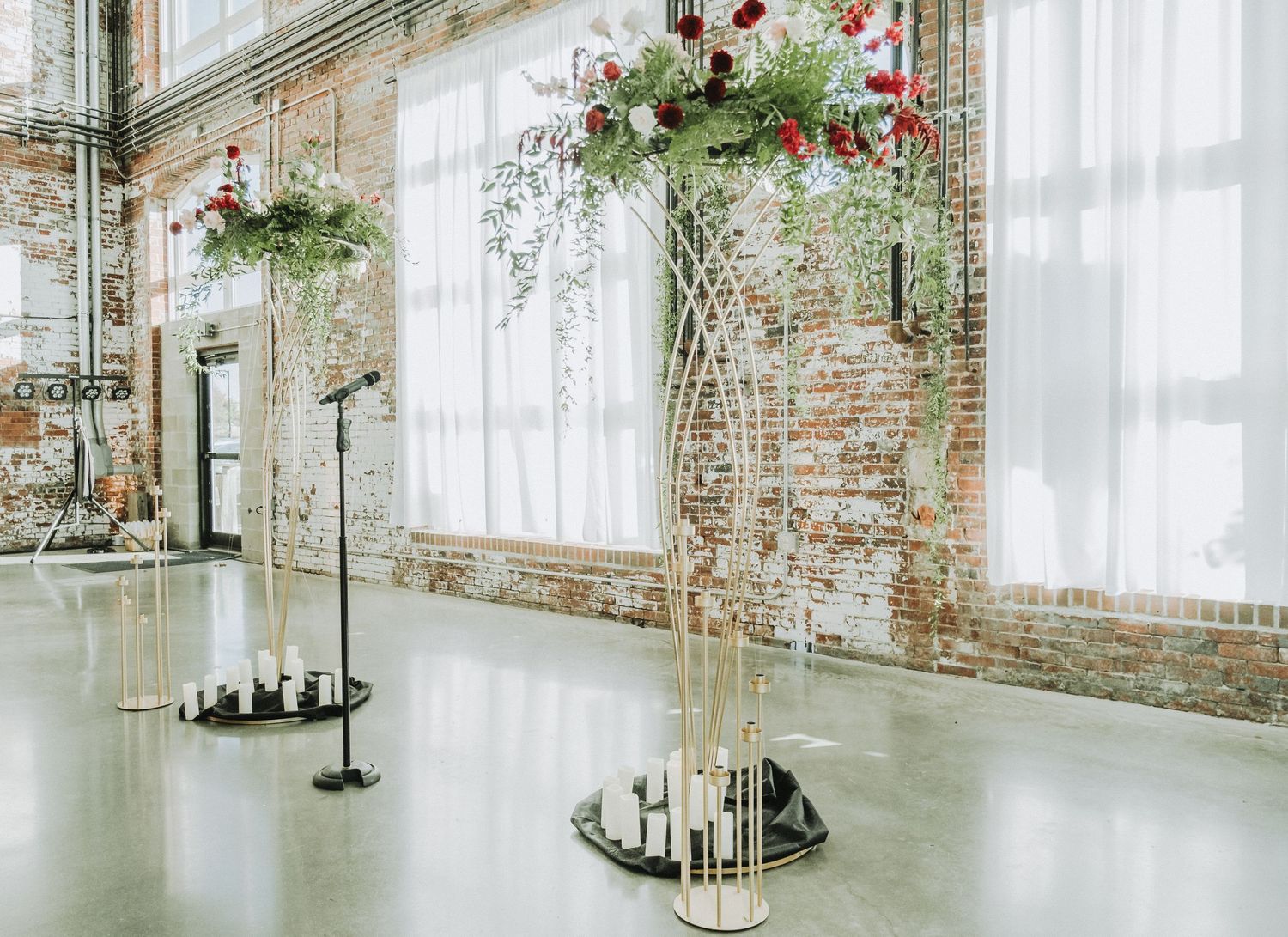 Industrial chic event space with exposed brick walls, tall windows, and elegant floral arrangements on mirrored pedestals.