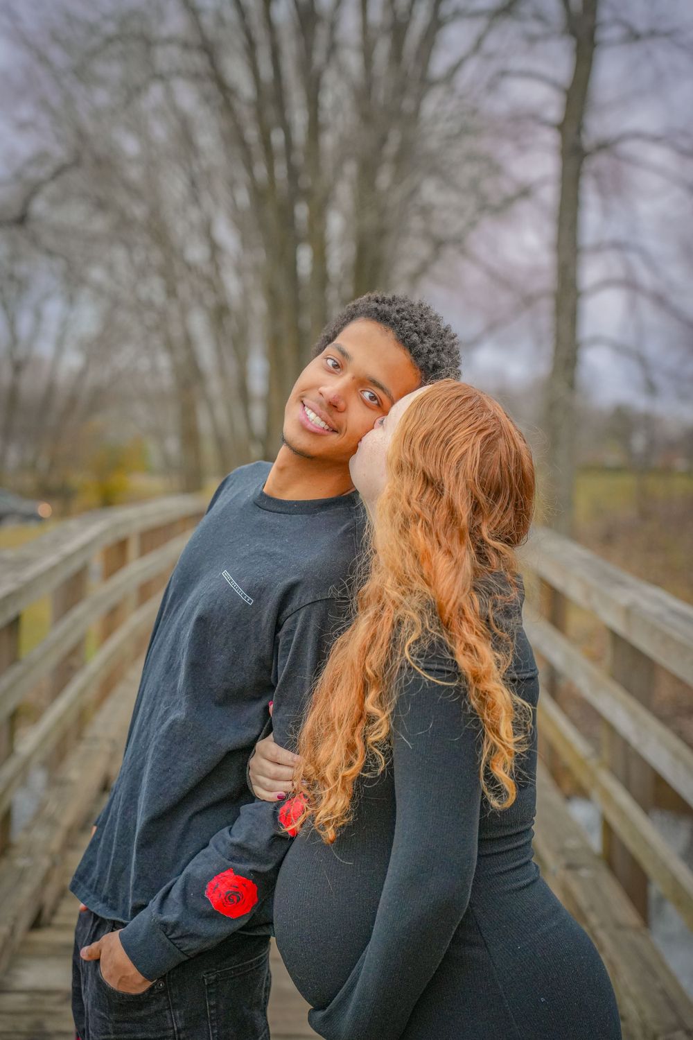 Couple sharing tender moment on wooden bridge during maternity photoshoot.