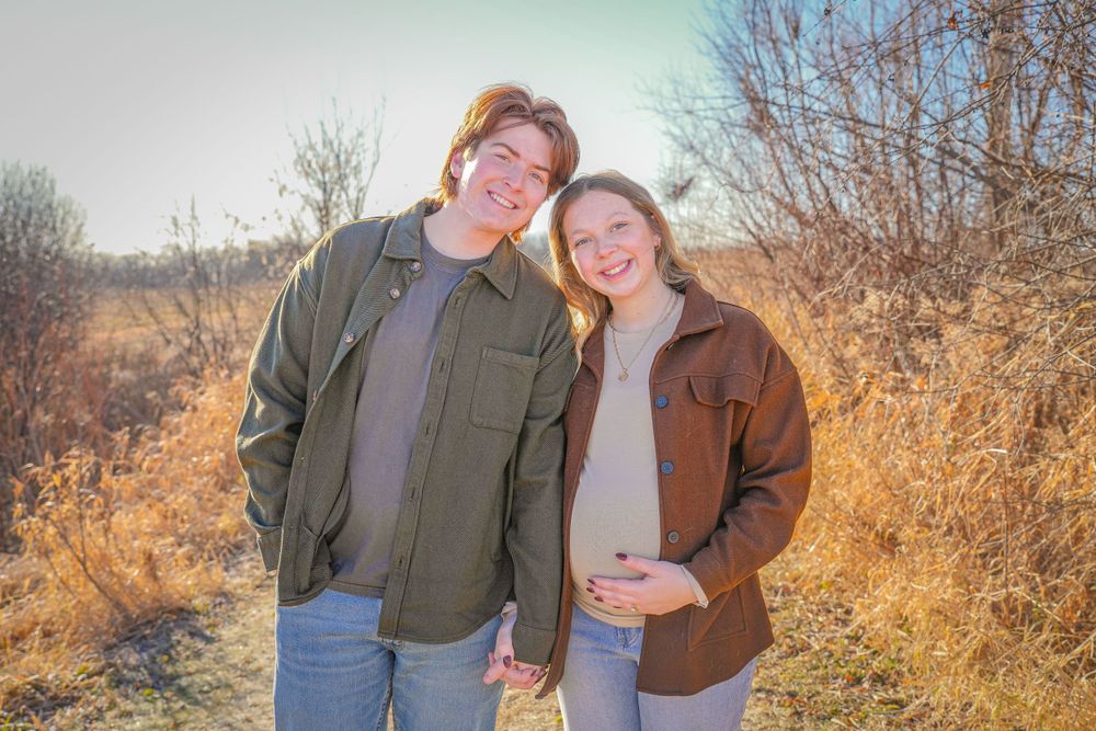 Couple posing together outdoors with golden grass and bushes in the background.