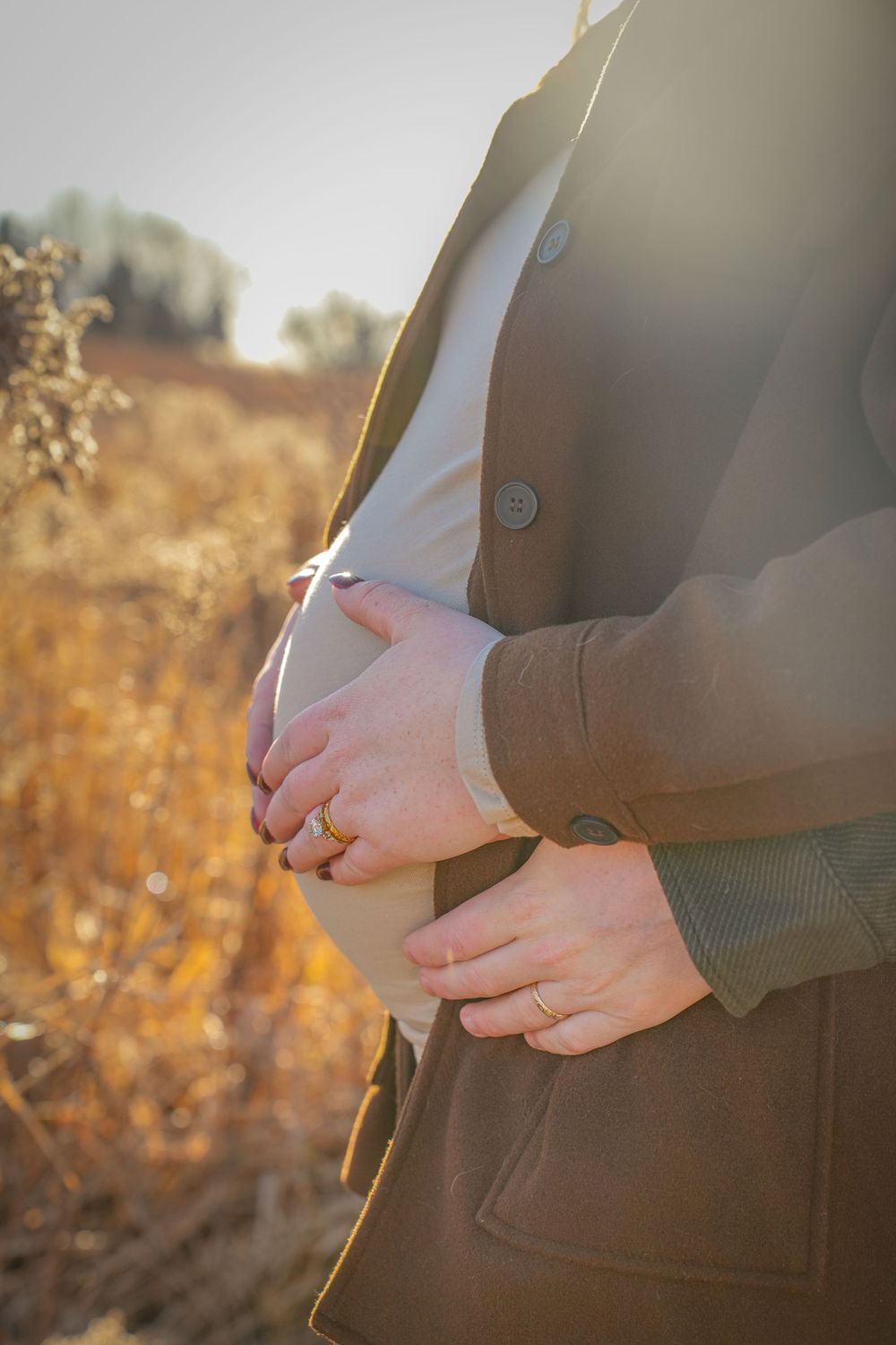 Person wearing brown coat with hands placed on stomach in golden sunlight.