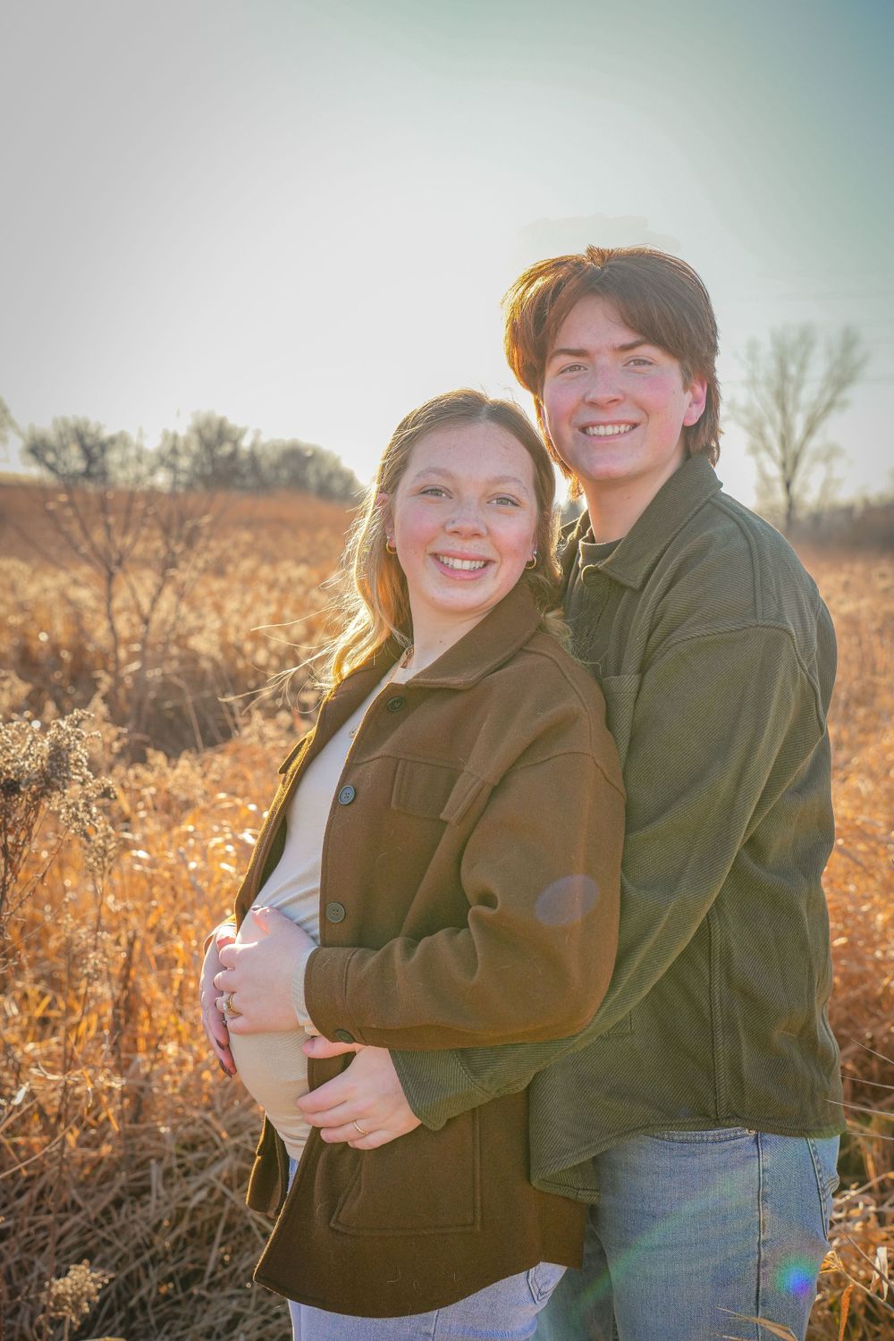 Couple embracing in a field during golden hour with autumn colors in background.