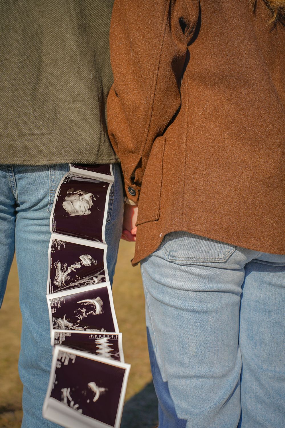Close-up of ultrasound photos being held between two people wearing jeans and brown coat.