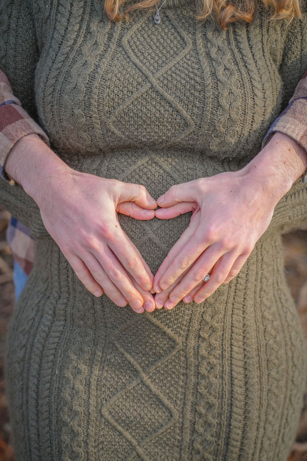 Hands forming heart shape over green knit sweater dress.