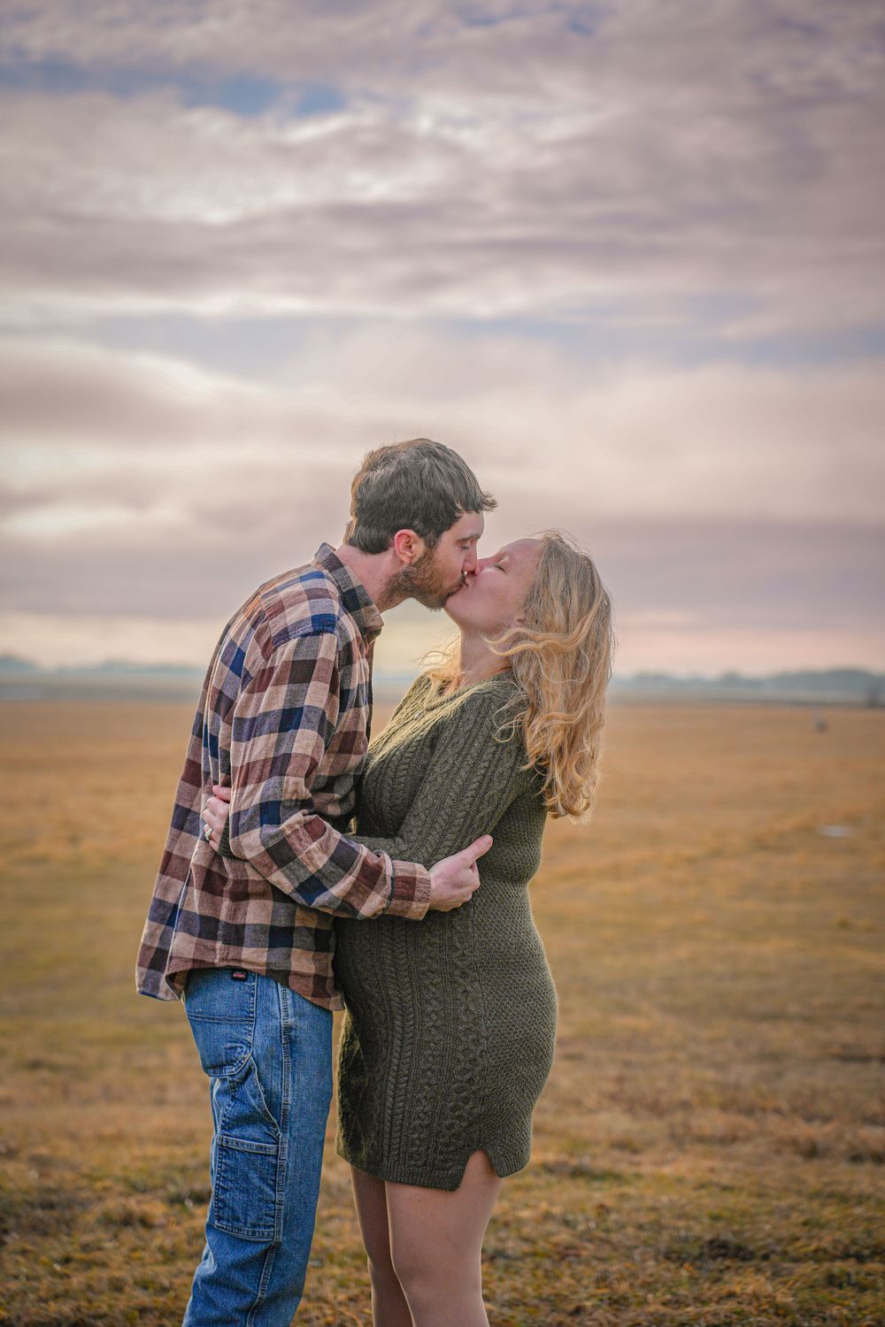 Romantic couple embracing in prairie field during sunset.