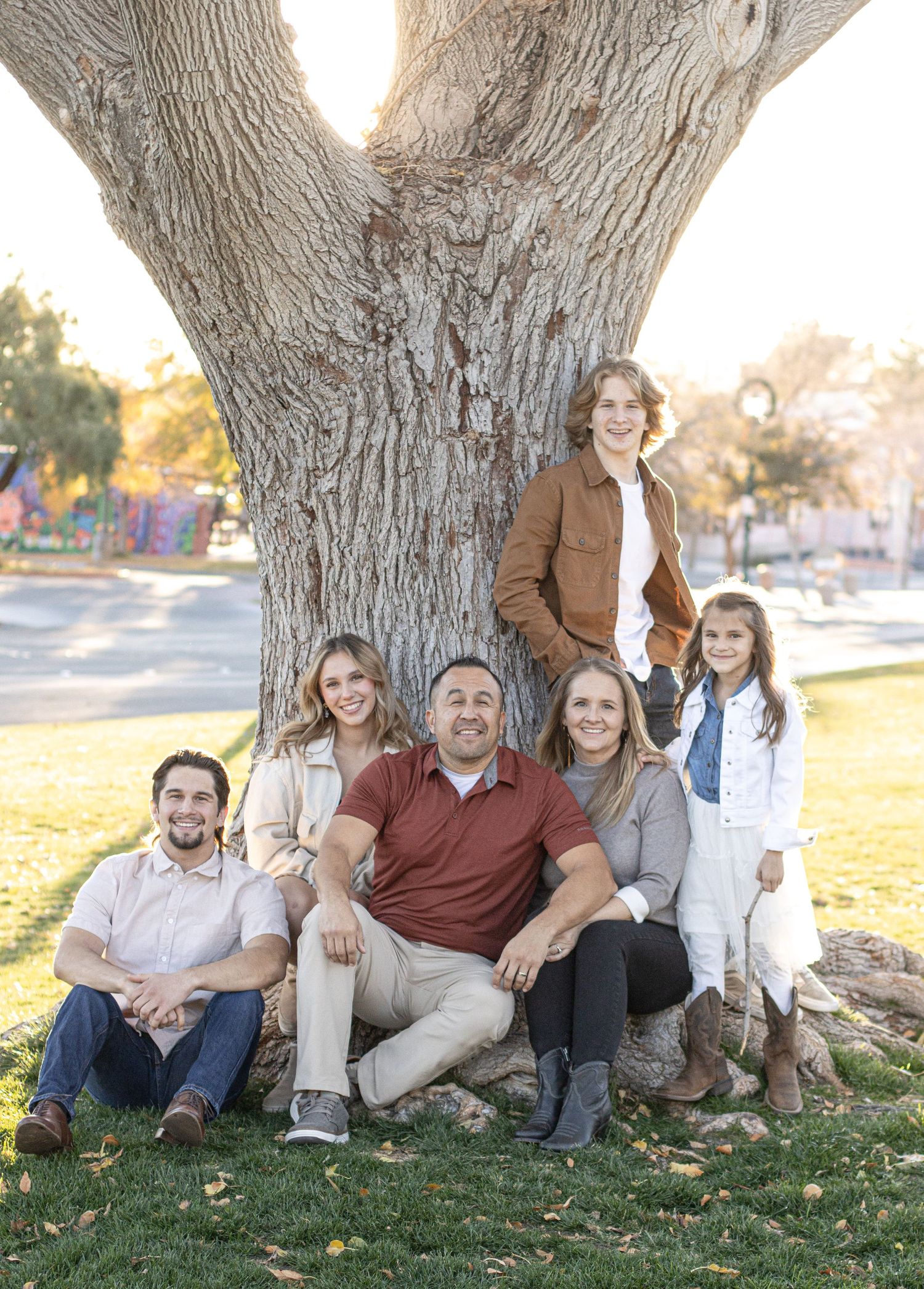 Cora Emilie Media -A family group sitting together at the base of a large tree in a park setting.