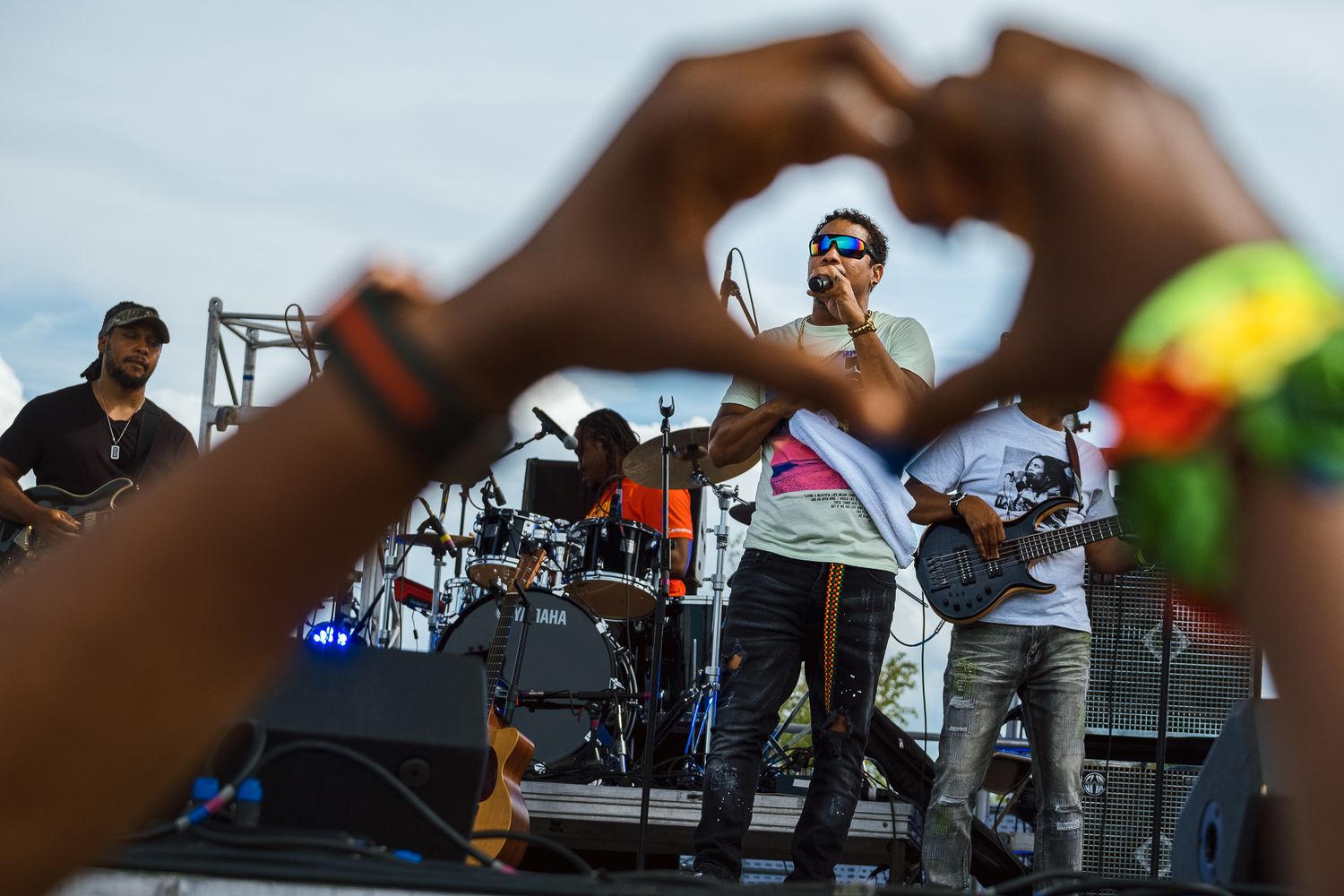 Concert audience making heart shapes with hands during an outdoor music performance.