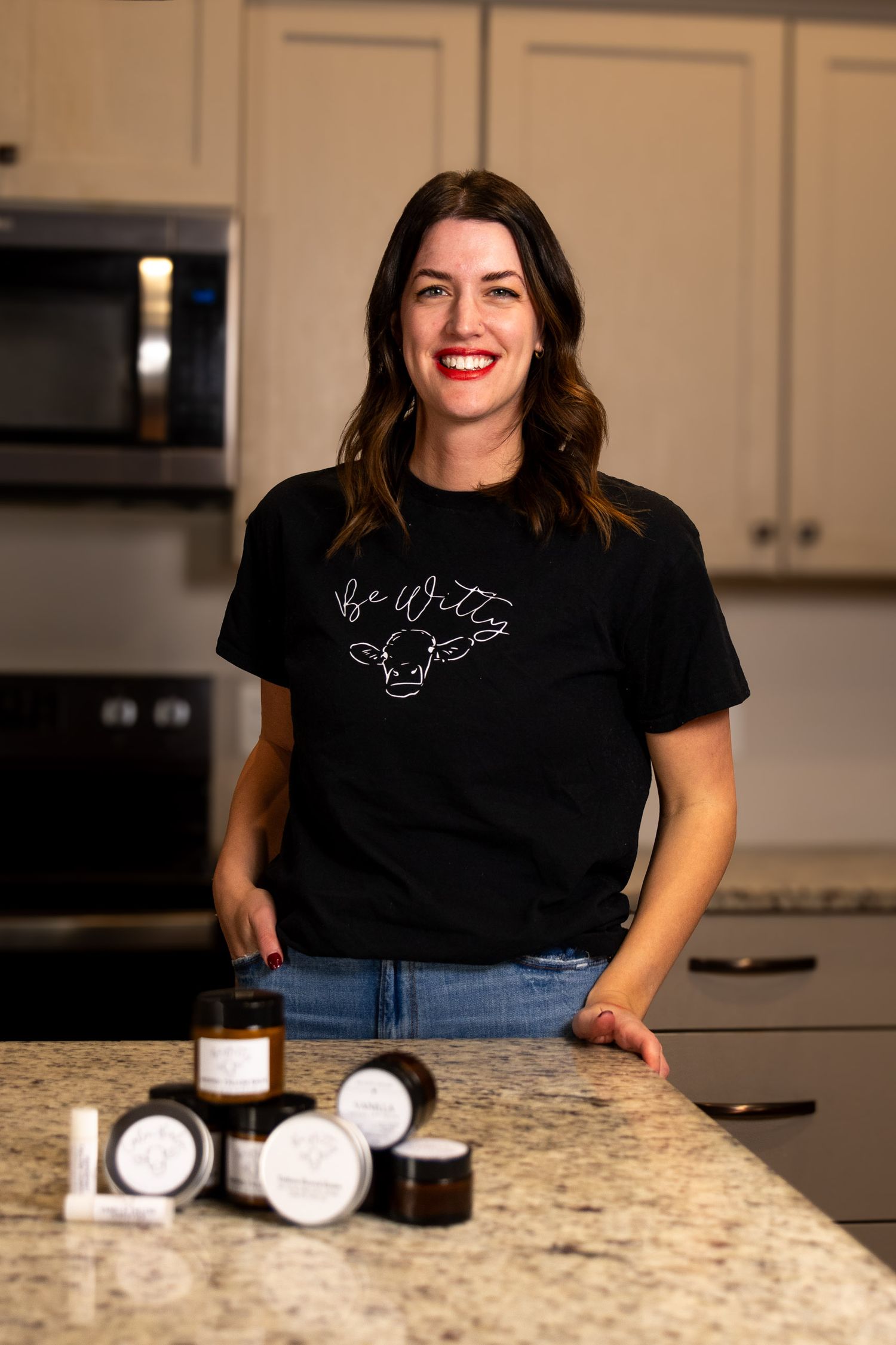 Person in black t-shirt with text graphic stands at kitchen counter with jars displayed.