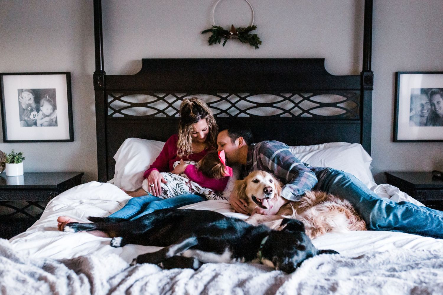 A family relaxes together with their golden retriever dog on a white bed with framed photos on the wall. Whitney Popp photographer