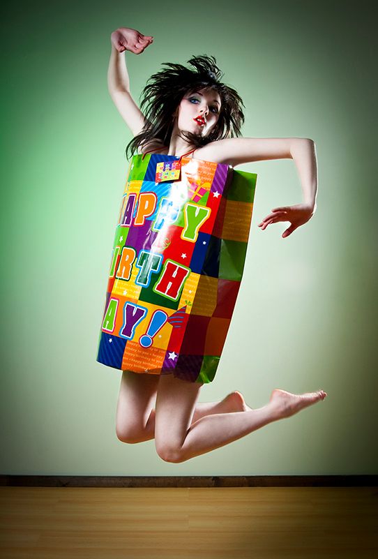 Energetic studio shot with person wearing a colorful block patterned dress jumping against green background.