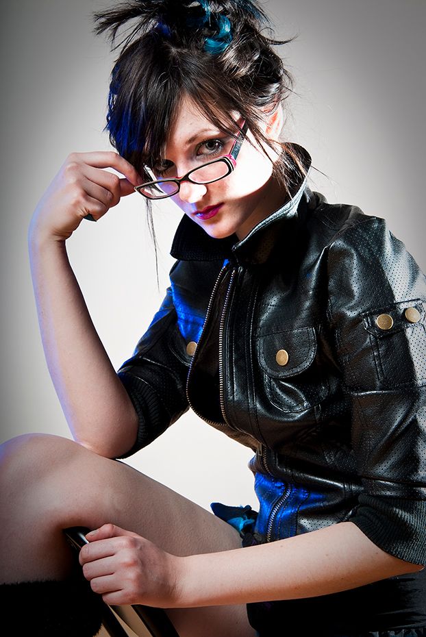 Artistic fashion portrait with dark leather jacket, glasses, and blue accents in studio lighting.