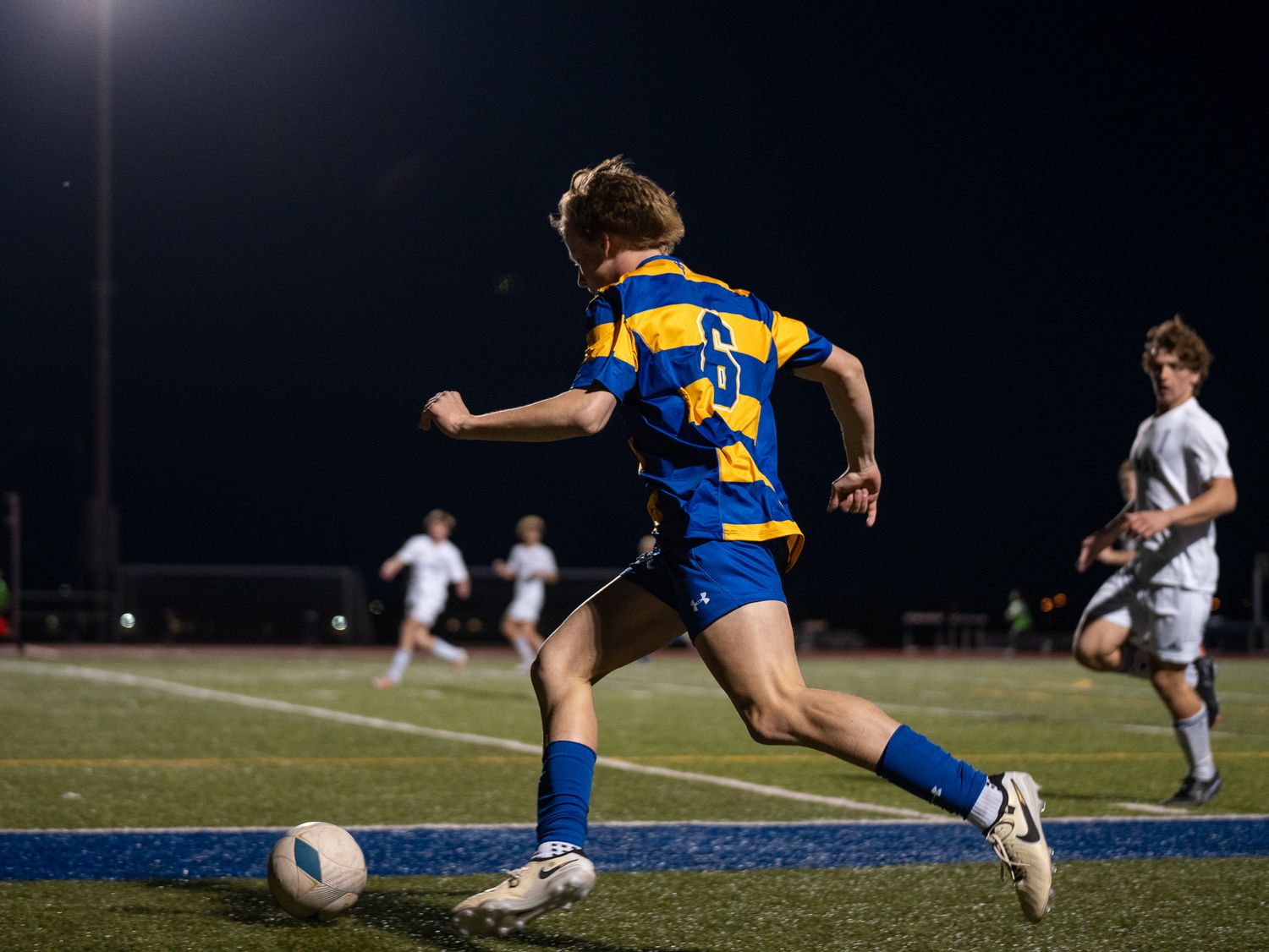 Soccer player in blue and yellow uniform dribbles ball during nighttime match.