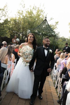 Newlyweds walking down the aisle after their ceremony on a brick patio.