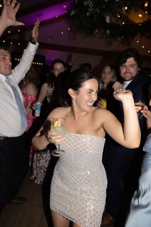 Wedding guests dance and celebrate on a purple-lit dance floor during an indoor reception.