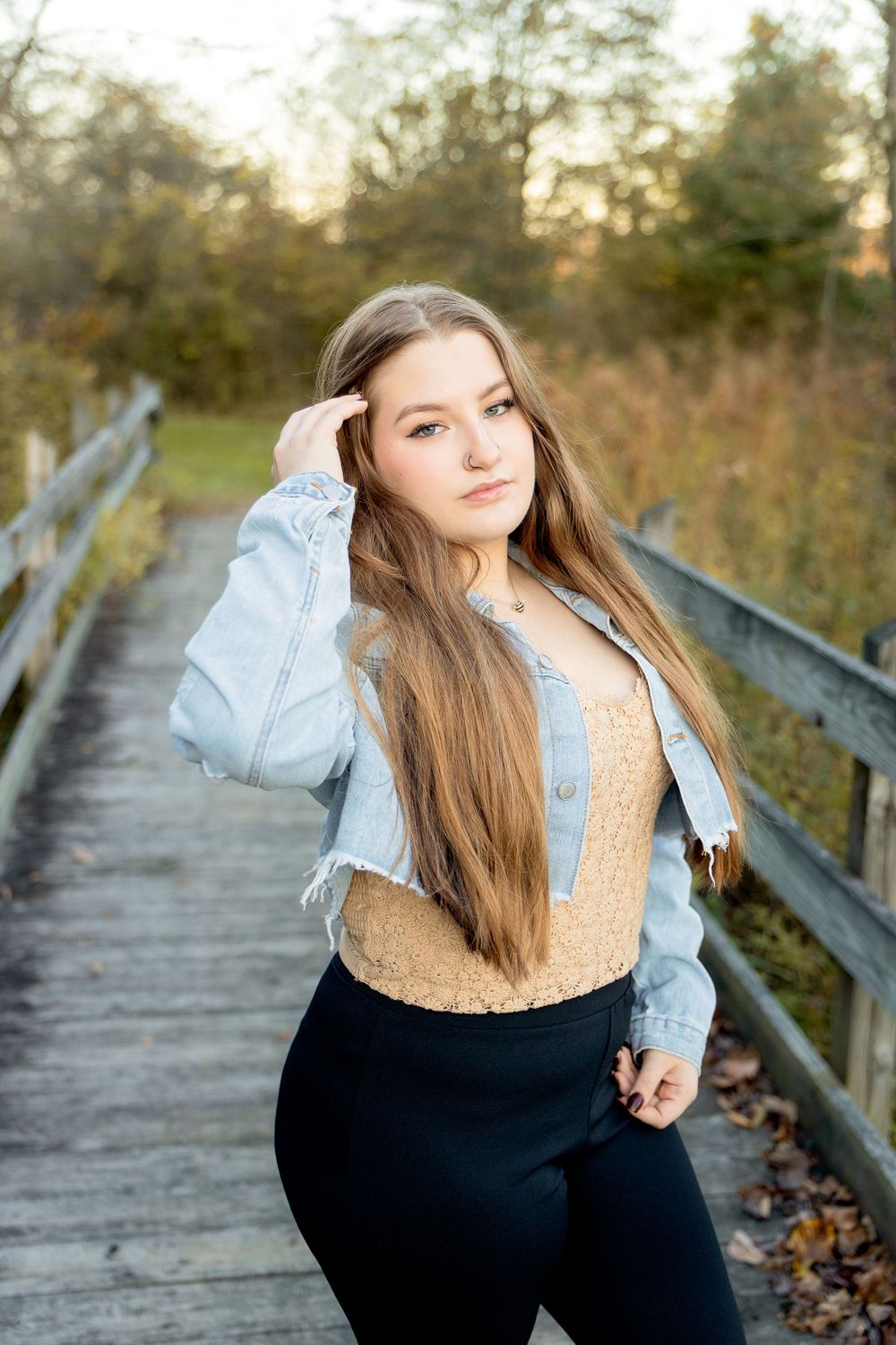 A casual autumn portrait on a wooden boardwalk showing a senior in a denim jacket and tan top against a golden hour background.
