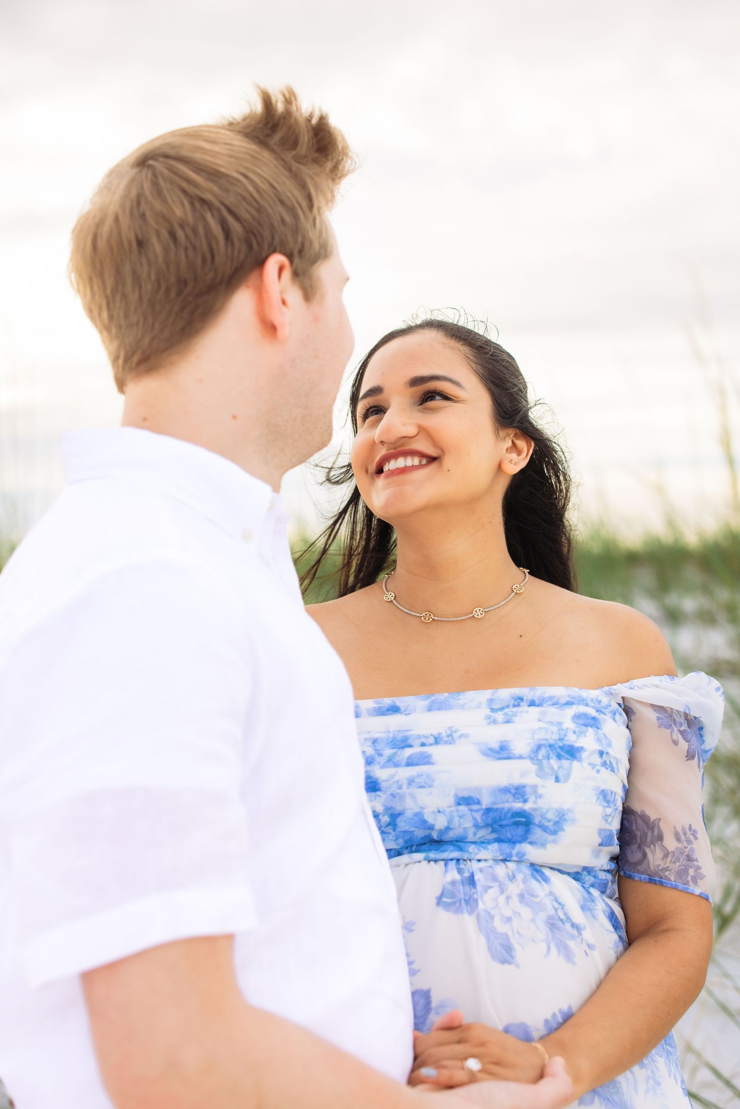 Couple sharing intimate moment on beach in white and blue attire.