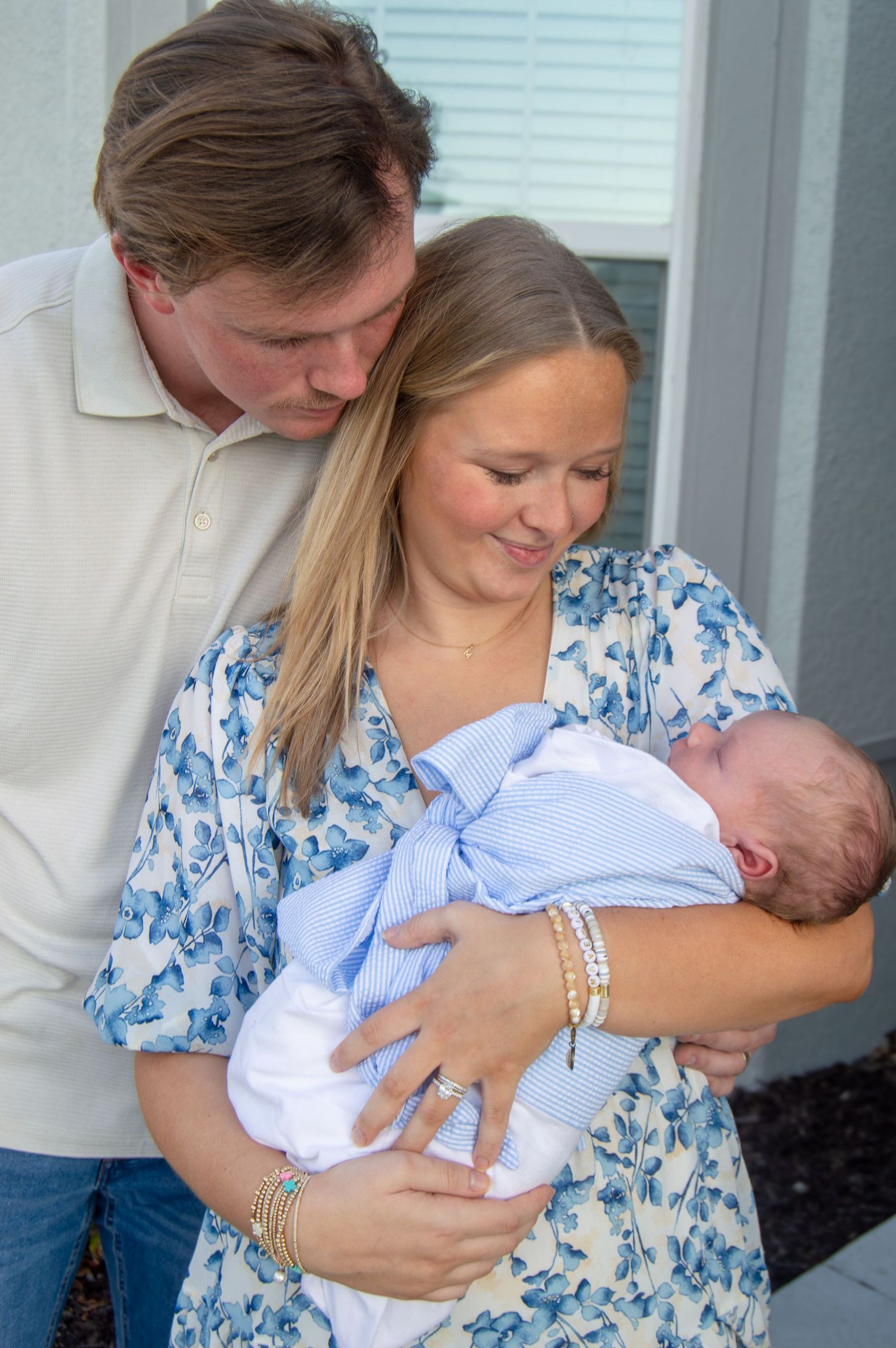 New parents lovingly gazing at their sleeping newborn baby wrapped in white blanket.