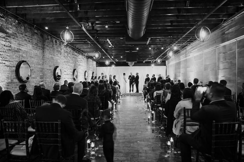 A black and white wedding ceremony in an industrial venue with exposed brick walls and string lights.