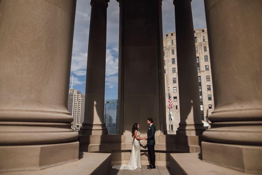 Bride and groom stand between massive stone columns during their wedding ceremony.