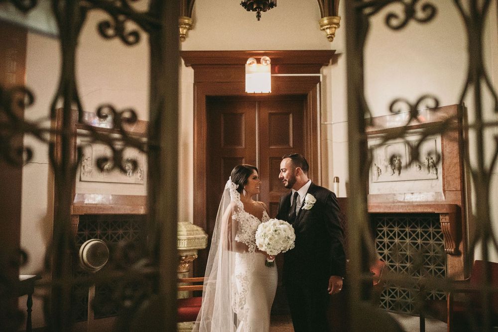A couple shares a wedding moment in an ornate church hallway with decorative ironwork.