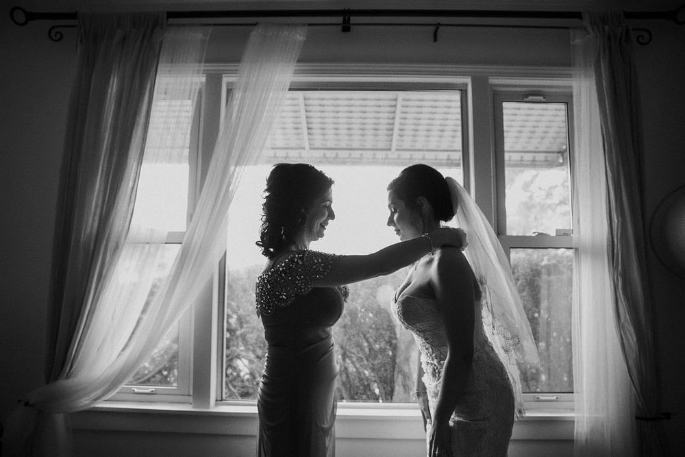 A black and white image showing wedding dress preparation by a window.